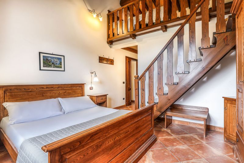 Camera con il letto matrimoniale, il pavimento in cotto e la scala in legno che sale al soppalco