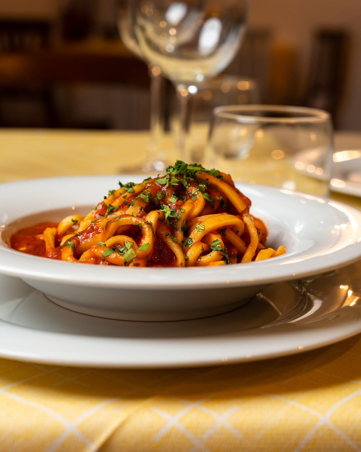 Un piatto di pasta fatta in casa al sugo di pomodoro, con i calici sul tavolo