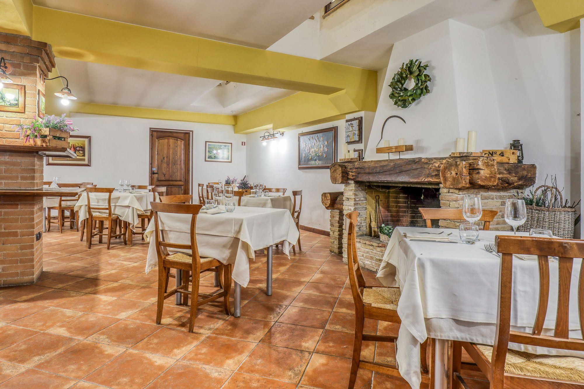 La sala con il camino in pietra e la trave di legno, i tavoli apparecchiati e la ghirlanda alla parete