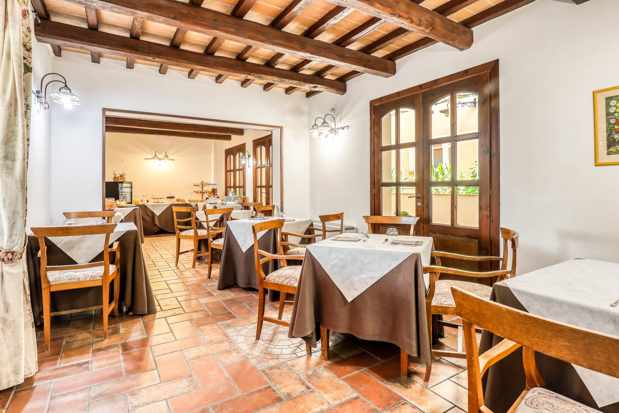 Sala del ristorante con travi a vista, pavimento in cotto e tavoli apparecchiati