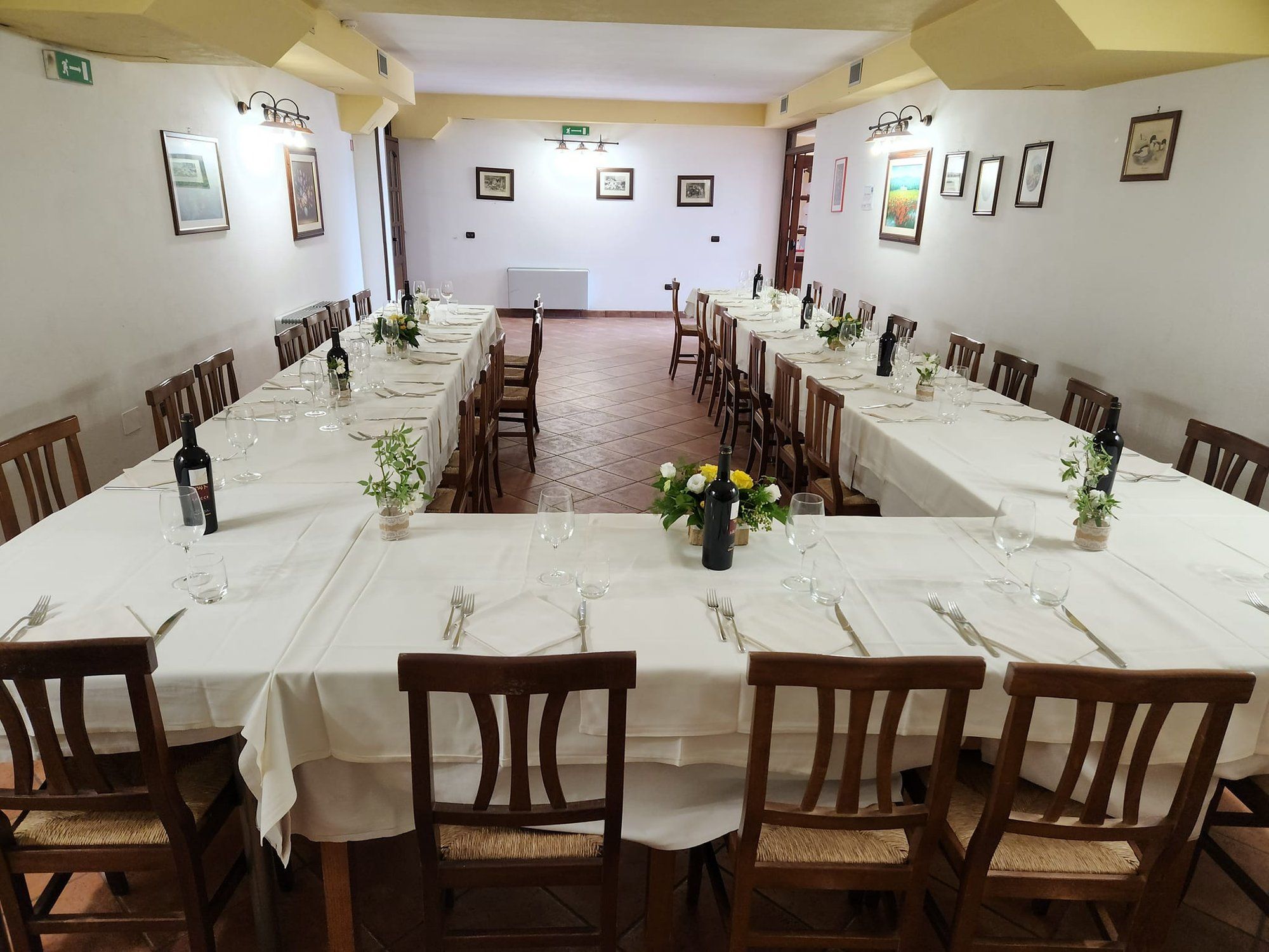 Una lunga tavolata apparecchiata per una festa nella sala del ristorante, con fiori e bottiglie di vino