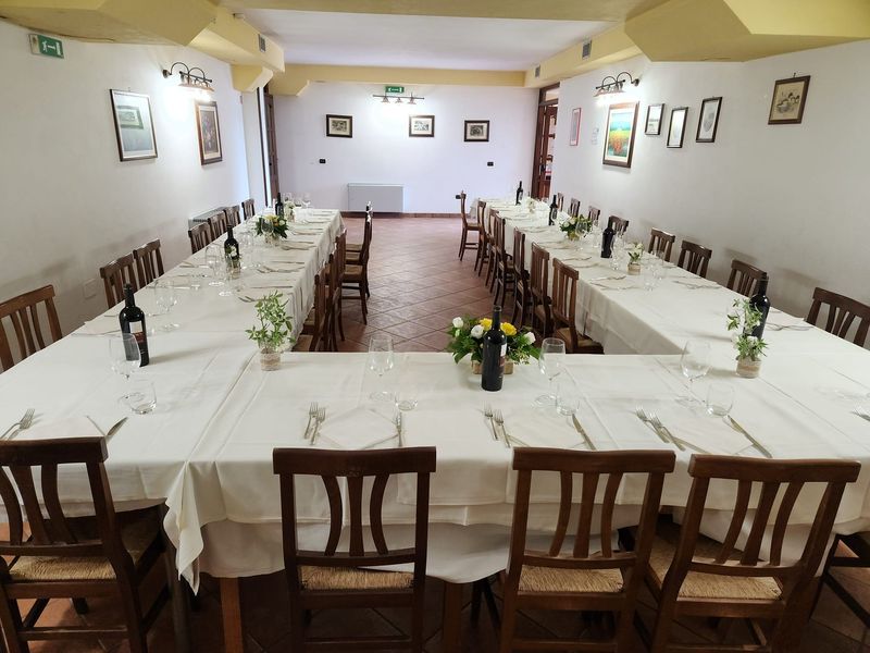 Una lunga tavolata apparecchiata per una festa nella sala del ristorante, con fiori e bottiglie di vino