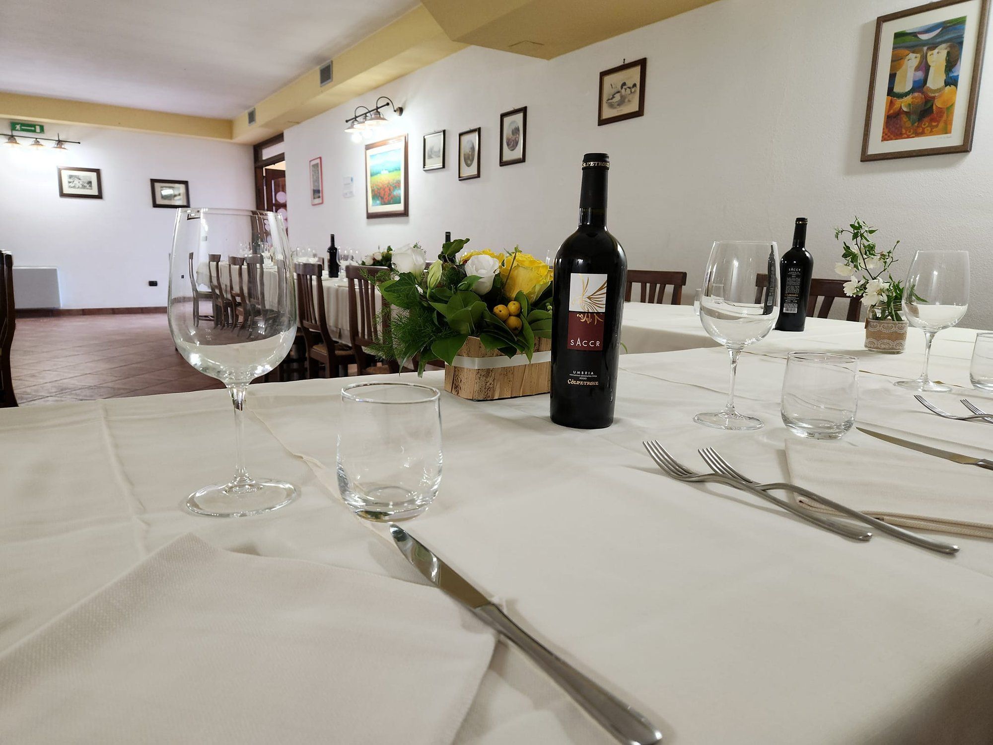 Calici e una bottiglia di vino rosso umbro su una tavola apparecchiata, con la sala sullo sfondo