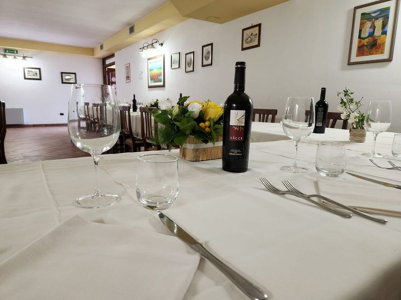 Calici e una bottiglia di vino rosso umbro su una tavola apparecchiata, con la sala sullo sfondo