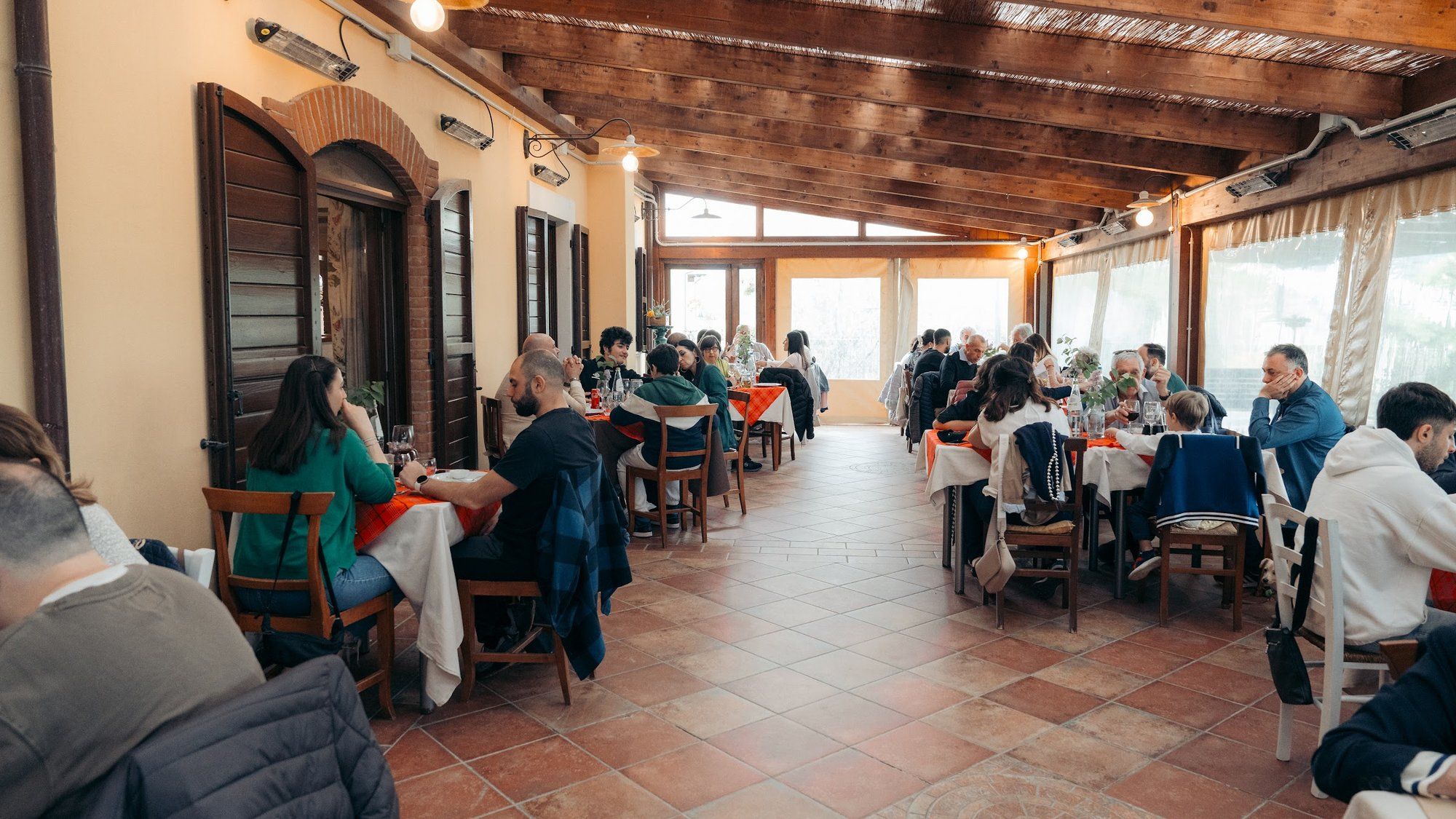 La veranda piena di famiglie a pranzo, con i tavoli apparecchiati di rosso