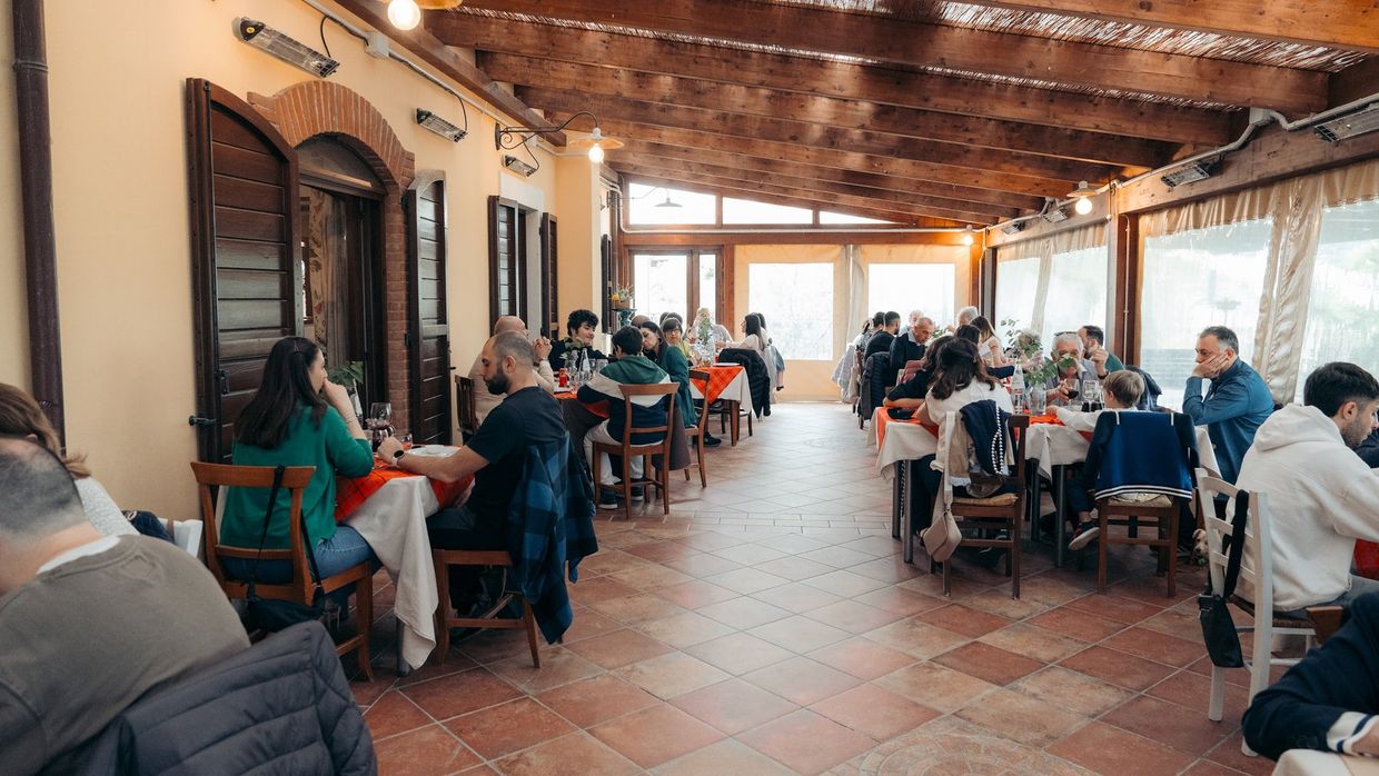 La veranda piena di famiglie a pranzo, con i tavoli apparecchiati di rosso