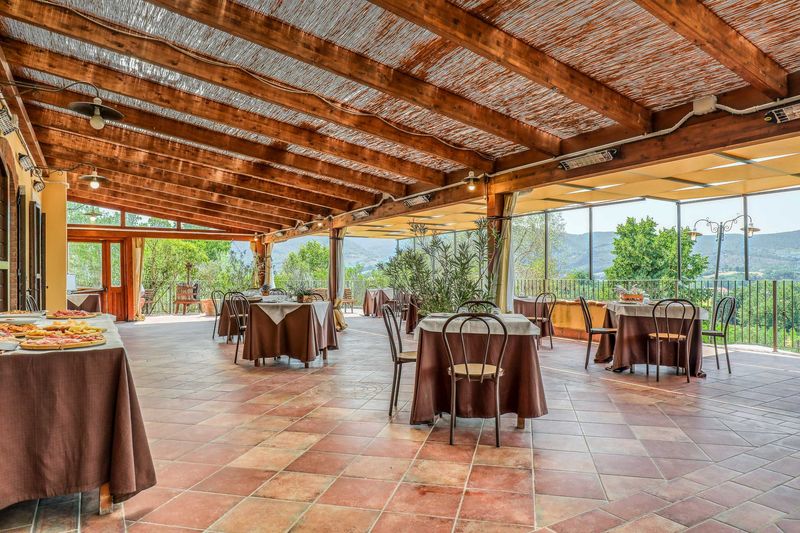 La veranda coperta con il soffitto in legno, i tavoli apparecchiati e la vista sulle colline